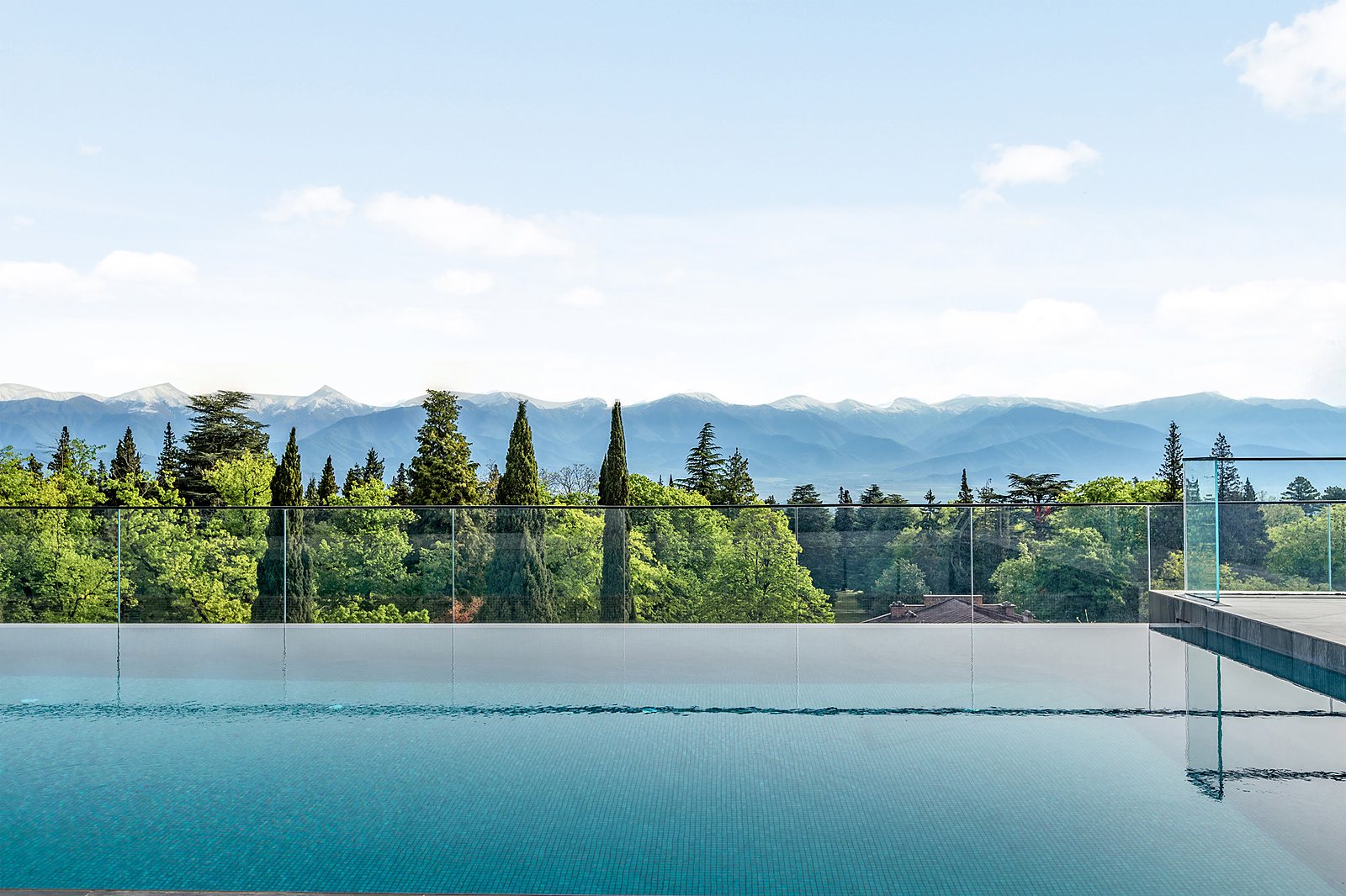 Rooftop infinity pool overlooking cypress trees and the snow-capped Greater Caucasus Mountains